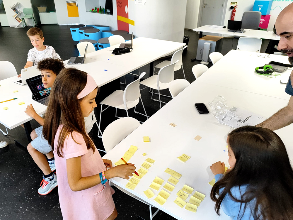 Image of children and an adult (myself, Pedro Rodrigues) on a workshop with post it notes, tables colorful seats and an iPad. This is an image related to a project inside Pedro Rodrigues (Treze413) graphic design portfolio.